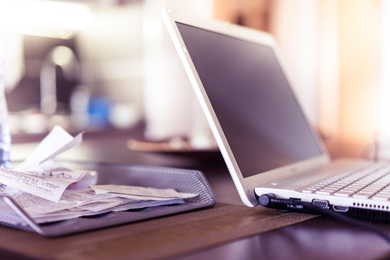 Mesh tray of paper receipts beside an open laptop on a desk